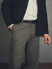 Person wearing a dark jacket, checkered shirt, and gray pants against a plain background