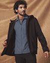 Man wearing a black jacket over a blue shirt against a brown background
