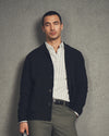 Man wearing a dark cardigan over a striped shirt against a gray background