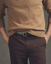 Person wearing a brown sweater and dark pants against a gray background