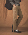 Person wearing beige pants and black shoes against a brown background