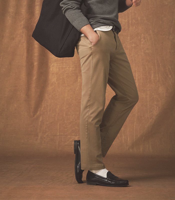 Person wearing beige pants and black shoes against a brown background