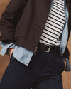Person wearing a dark jacket, striped shirt, and jeans with a brown background