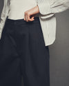 Person wearing a white shirt with a striped pattern and dark pants against a gray background