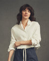 Woman wearing a white shirt and dark pants against a gray background