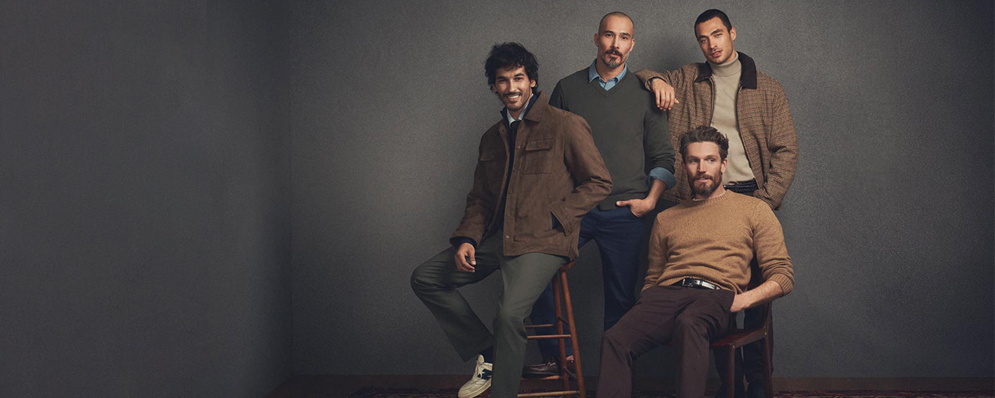 Four men posing together against a dark gray background