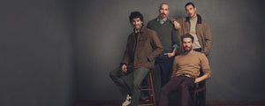 Four men posing together against a dark gray background