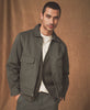 Man wearing a green jacket over a white shirt against a brown background