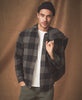 Man wearing a plaid shirt over a white t-shirt with a brown background